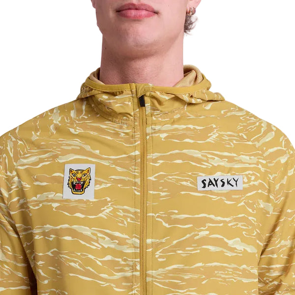 En person iført Saysky Tiger Pace Jacket, Herre, Yellow Camo - en gul og hvid tigerstribet løbejakke med hætte, vindbeskyttelse, et snerrende tigerhovedmærke og et Saysky-brystmærke.