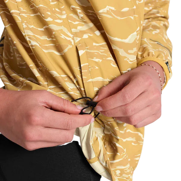 En person justerer den sorte løbegang nederst på Saysky Tiger Pace Jacket, Dame, Yellow Camo, med kun hænder og overkrop synlige.