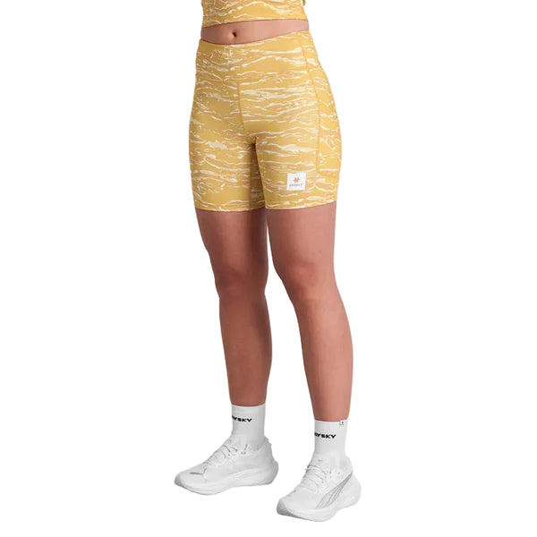 En person bærer Saysky Tiger Combat+ Short Tights 7", Dame, Yellow Camo med en matchende crop top, hvide strømper og sportssko på en hvid baggrund. Ansigtet er ikke synligt.