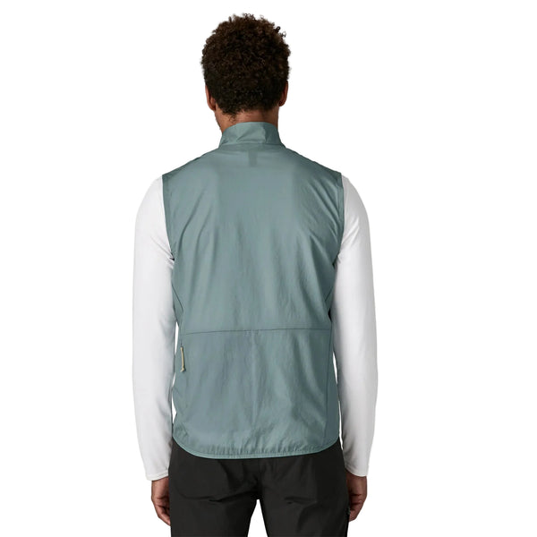 En person ses bagfra iført en Patagonia Trail Craft Vest, Herre, Blue Sage over en hvid langærmet skjorte og sorte bukser på en almindelig hvid baggrund.