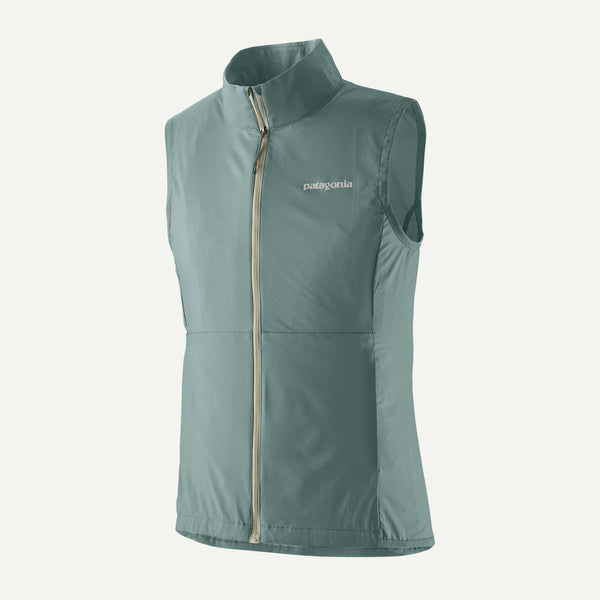 Patagonia Trail Craft Vest, Dame i Blue Sage, har lynlås foran og opretstående krave med logo på venstre bryst - en let ultralet løbevest, der er perfekt til udendørs eventyr, vist på en almindelig hvid baggrund.
