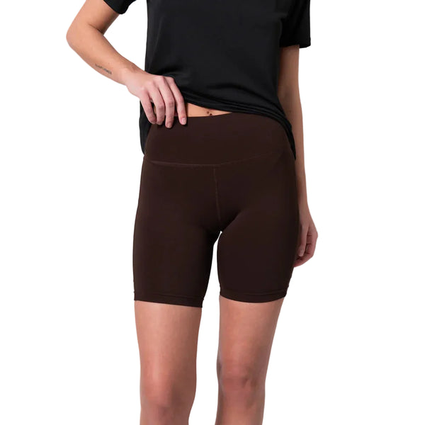 En person iført en sort kortærmet T-shirt og Liiteguards »Training Tights Short, Dame« i farven »Coffee Bean« står foran en ensfarvet hvid baggrund og løfter let T-shirtens nederste kant med den ene hånd. De elegante tights med høj talje skaber en flatterende silhuet, der er perfekt til både hverdagsbrug og træning for kvinder.