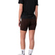 En person står med ryggen til kameraet og er iført en sort T-shirt, Liiteguard Training Tights Short, Dame i farven Coffee Bean, hvide sokker med sort mønster og hvide sko, foran en hvid baggrund.