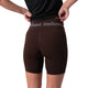 En person iført en sort T-shirt og Liiteguards »Training Tights Short, Dame, Coffee Bean« – hvor Liiteguard-logoet er synligt på linningen – står med ryggen til og retter på linningen med hænderne, hvilket fremhæver den perfekte pasform, der er typisk for højtaljede tights designet til kvinders træning.