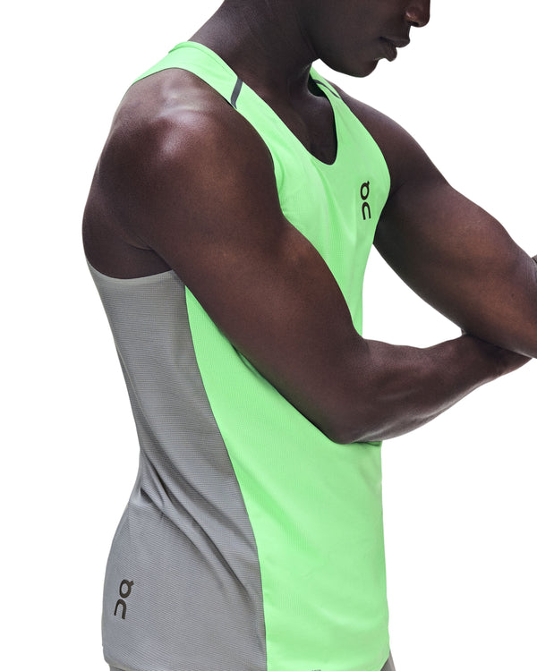 En person iført ON Performance Tank til mænd i farvekombinationen Verdite/Apollo – en ærmeløs sportstop med neongrøn front og grå sider med ON-logoet – poserer med krydsede arme foran en ensfarvet hvid baggrund.
