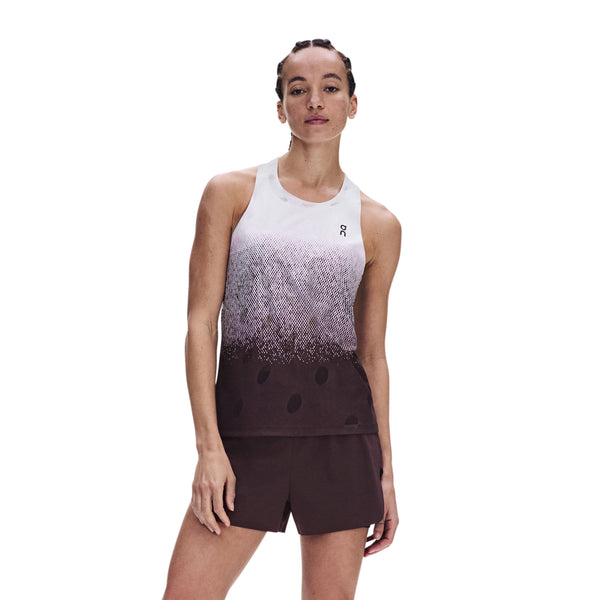 En person står med ansigtet vendt fremad og har ON Zero Tank Breath, Dame i farven Foxglove/White på – en ærmeløs sports-tanktop – samt mørkebrune sportsshorts. Baggrunden er ensfarvet hvid.
