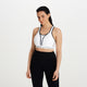 En kvinde med langt mørkt hår bærer Shock Absorber Ultimate Run Bra Padded, Dame, White og sorte højtaljede leggings. Hun står med ansigtet fremad og et neutralt udtryk mod en almindelig hvid baggrund.
