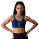 En kvinde med langt krøllet hår bærer Shock Absorber Ultimate Run Bra Padded, Dame, i Sail Away Navy, mens hun står med hænderne på hofterne mod en hvid baggrund.
