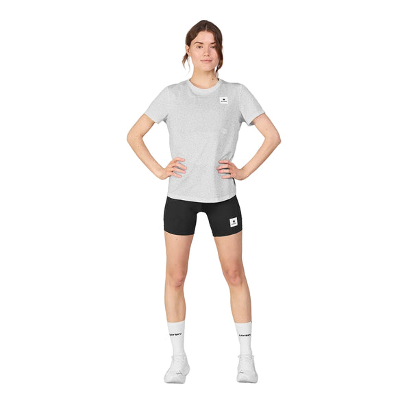 En person står på en hvid baggrund iført Saysky Universe Combat T-Shirt, Dame, White Universe, sorte shorts, hvide sokker og hvide sneakers med hænderne på hofterne.