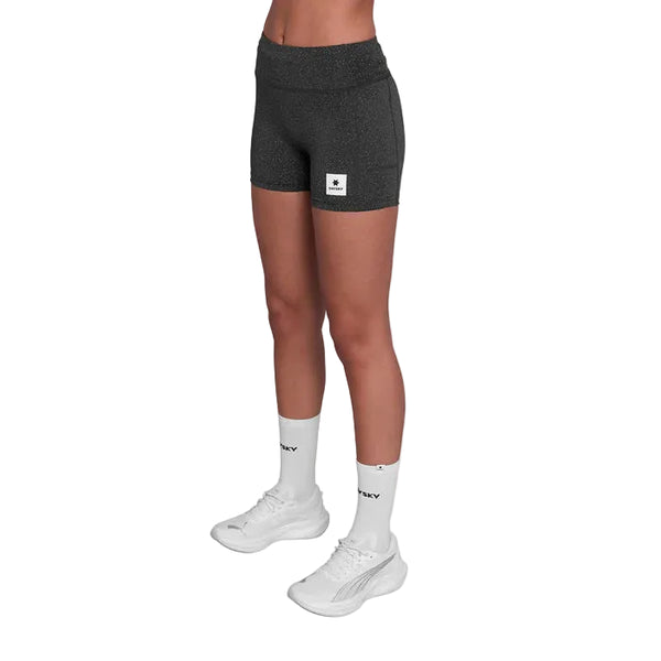 En person er iført sorte Saysky Universe Combat+ Short Tights 4" (Dame, Black Universe) sammen med hvide strømper med sort tekst og hvide løbesko. Strømpebukserne har et lille rektangulært logo på venstre ben.