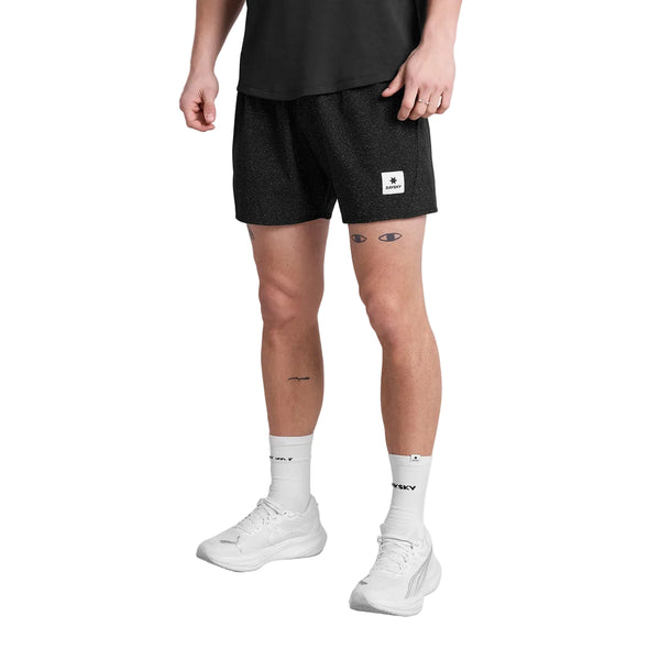 En person iført sort t-shirt, Saysky Universe Pace Shorts 5" Herre Black Universe med hvid logopatch, hvide strømper med sort skrift og hvide sneakers står på en almindelig hvid baggrund.