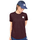 En person iført en Saysky Clean Combat Pro-T-shirt, Dame, i farven burgundy med et logo-mærke, kombineret med blå shorts og en blå kasket med et matchende logo-mærke, står med den ene arm bag ryggen og kigger ned.