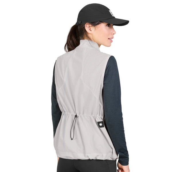 En person iført en sort kasket, en mørk langærmet trøje og Saysky W Clean Pace Flex-vesten (Dame, grå) står med ryggen til kameraet. Den lysegrå vest har elastiske mesh-paneler, der giver ekstra komfort og åndbarhed, samt en snøre bagpå og et lille stjerne-mærke tæt på taljen.