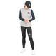En person iført en sort kasket, en grå Saysky W Clean Pace Flex Vest til kvinder, en sort langærmet trøje med paneler af stretchmesh, sorte leggings og hvide sneakers står foran en hvid baggrund og ser ned med hænderne foldet foran sig.