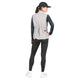 En kvinde iført Saysky W Clean Pace Flex Vest, Dame, grå – med elastiske mesh-paneler, der sikrer god åndbarhed – samt en sort langærmet bluse, sorte leggings, hvide sneakers og en sort kasket står med ryggen til og den ene hånd på hoften.
