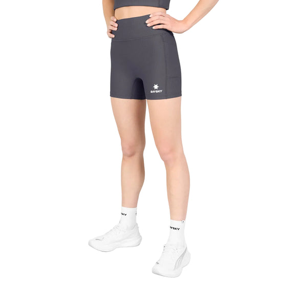 En person står med hænderne i siden og har Saysky W Combat+ Rib Short Tights 4″ til kvinder i gråt på – fremstillet af åndbart ribstof – kombineret med en matchende top, hvide sokker med sort tekst og hvide sportssko på en ensfarvet hvid baggrund.