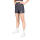 En person står med hænderne i siden og har Saysky W Combat+ Rib Short Tights 4″ til kvinder i gråt på – fremstillet af åndbart ribstof – kombineret med en matchende top, hvide sokker med sort tekst og hvide sportssko på en ensfarvet hvid baggrund.