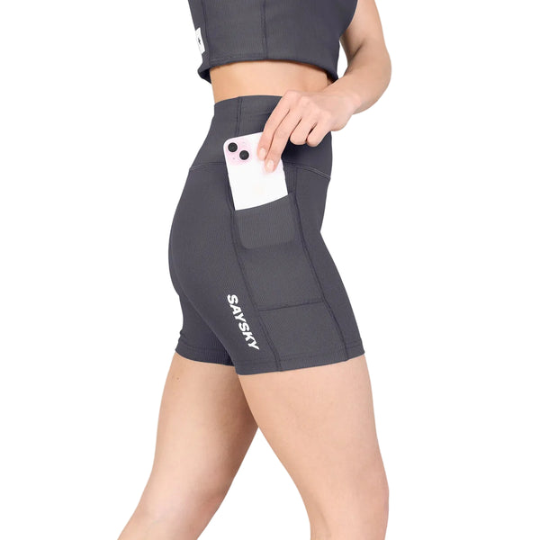 Man ser en person iført et par W Combat+ Rib Short Tights 4″, Dame, Grå fra Saysky, der er fremstillet af åndbart ribstof og har en praktisk sidelomme. Personen lægger en hvid smartphone ned i lommen, og Saysky-mærket kan ses på shortsenes venstre ben. Personens overkrop er delvist synlig.
