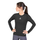 En kvinde med mørkt hår i hestehale har en Saysky W Combat Tech Long Sleeve, Dame, Black på – en sort langærmet sportstrøje, der er kombineret med grå leggings. Hun står med hænderne på hofterne og kigger til venstre. T-shirten er fremstillet af svedtransporterende løbetøj og har en lille hvid stjerne samt Saysky-logoet på brystet.