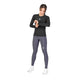 En kvinde står foran en hvid baggrund iført den sorte Saysky W Combat Tech Long Sleeve til kvinder, kombineret med grå leggings og hvide sko. Hun kigger på sit håndled, som om hun tjekker sit ur. Dette svedtransporterende løbetøj fra Saysky sikrer, at hun forbliver komfortabel og tør under enhver aktivitet.