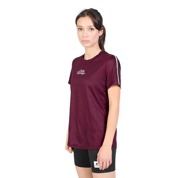 En kvinde står med ansigtet vendt fremad iført en Saysky W Couture Combat T-shirt, model »Dame« i farven »Burgundy Aop«, med tekst på brystet, kombineret med sorte shorts med et lille hvidt mærke. Hun har langt, mørkt hår, der er sat op, og et neutralt udtryk i ansigtet. Baggrunden er ensfarvet hvid.