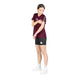 En person står på en hvid baggrund iført en Saysky W Couture Combat T-shirt, Dame, Burgundy Aop, kombineret med sorte shorts, hvide sokker og hvide sko. Personen kigger ned og rører ved sin overarm med den modsatte hånd.