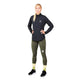 En person står foran en ensfarvet lysegrå baggrund iført Saysky W Blaze Half Zip Light-Weight Fleece til kvinder i sort – fremstillet af letvægts-løbefleece af genanvendt polyester – kombineret med olivengrønne leggings med lommer, gule sokker og sorte løbesko. Med hænderne på hofterne og blikket rettet fremad udstråler vedkommende et selvsikkert udtryk, der passer perfekt til aktive kvinder.
