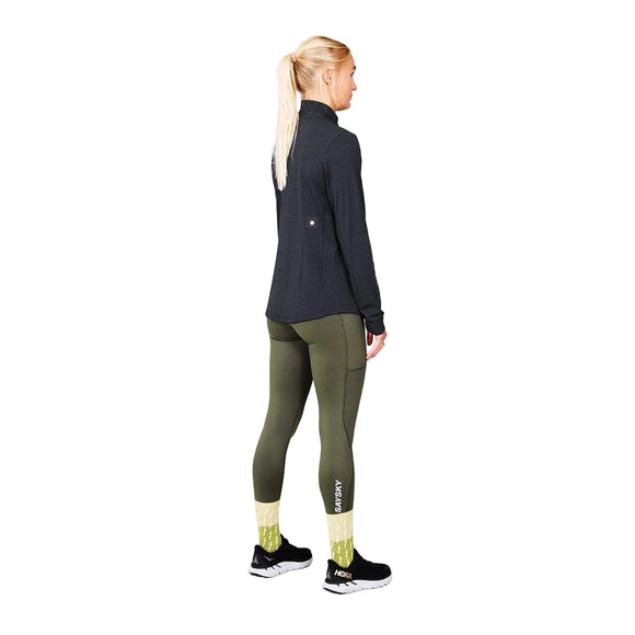 En kvinde med blondt hår i hestehale står med ryggen til; hun er iført en mørk langærmet bluse af genbrugt polyester, olivengrønne leggings med SAYSKY-logo, gule mønstrede strømper og sorte løbesko. Hendes stilfulde outfit til kvinder fuldendes af den funktionelle Saysky W Blaze Half Zip Light-Weight Fleece, Dame, Black – en elegant, letvægts løbefleece, der fremstår tydeligt mod en ensfarvet grå baggrund.