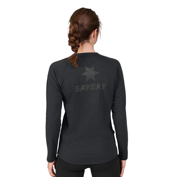 En kvinde med brunt hår i en fletning står med ryggen til kameraet og har en Saysky W Blaze langærmet, letvægtsfleece i sort på. Denne lette sportstrøje til kvinder er fremstillet af genanvendt polyester og har et diskret stjernemønster samt SAYSKY-logoet trykt på ryggen. Baggrunden er ensfarvet hvid.