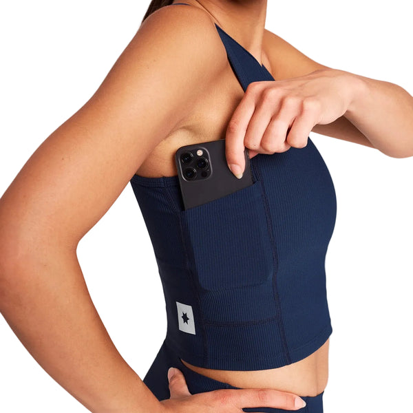En person iført en mørkeblå W Combat Rib Crop Top, der lægger en smartphone i sidelommen.