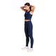 En person har en mørkeblå W Combat Rib Crop Top på samt matchende leggings med høj talje og hvide sportssko.