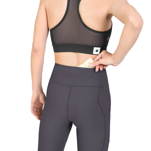 En person, der har en sort sports-BH og et par grå Saysky W Combat+ Rib Long Tights til kvinder på, lægger en pude i lommen i linningen bag på leggingsene.