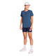 En person står foran en hvid baggrund iført en blå Saysky W Logo Combat Pro-T-shirt til kvinder, marineblå shorts, hvide sokker, hvide sko og en hvid kasket. Personen smiler og holder et lille kort i venstre hånd og ser afslappet og stilfuld ud i sit hurtigtørrende træningstøj.