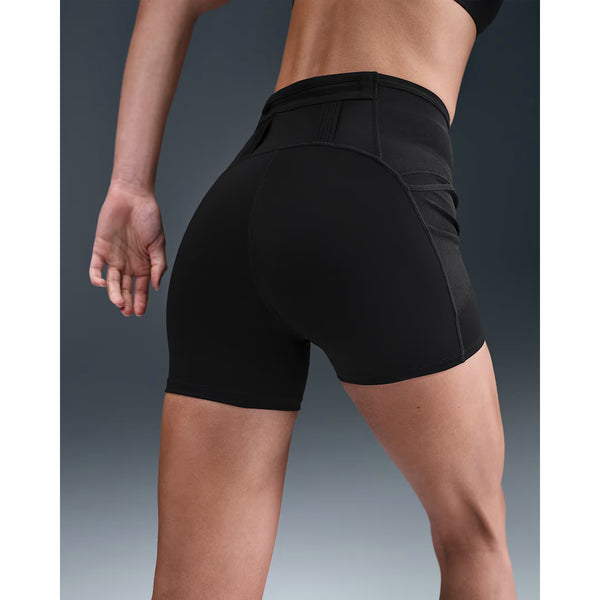 En kvinde iført Nike Dri-FIT High-Waisted 4" Tight Running Shorts i sort/sort og en sort sports-bh står med bøjet venstre arm. Baggrunden er en ensfarvet gradient, der går jævnt fra mørkt til lyst.