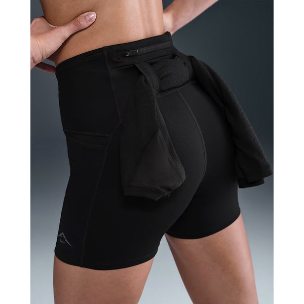 En person iført Nike Dri-FIT High-Waisted 4" Tight Running Shorts til kvinder i sort/sort, med en jakke bundet om livet, set bagfra mod en neutral baggrund.