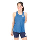 En kvinde står foran en hvid baggrund iført Saysky W Reactive Flow Singlet, Dame, Blue Aop – en ærmeløs sports-tanktop – kombineret med marineblå cykelshorts. Den ene arm hviler bag ryggen, mens hun kigger let til siden, hvilket fremhæver både singletens strømlinede pasform og den optimale svedtransporterende ydeevne, der sikrer træning med høj komfort.