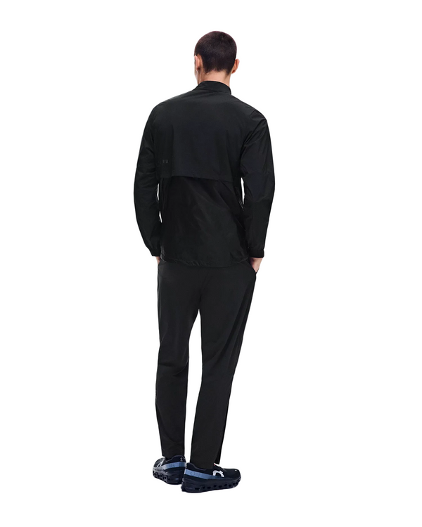 En person står med ryggen til, iført en sort jakke, et par sorte »On Weather Pants Herre« og sorte sko. Baggrunden er hvid, og personen har hænderne langs siden og hovedet let vendt mod højre.