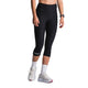En person i Fusion 3/4 Training Tights, Dame, SuperBlack, parret med et sort smartwatch, hvide sokker og hvide sportssko står på en almindelig lys baggrund. Billedet er beskåret ved skuldrene.