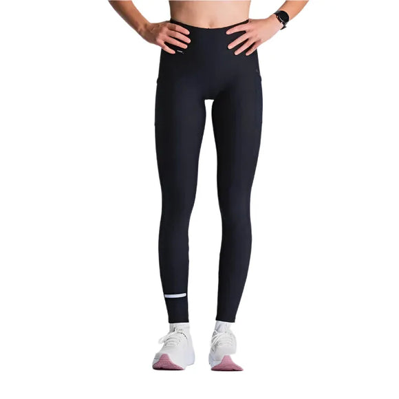 En person iført Fusion X-Long Training Tight, Dame, SuperBlack leggings står på en hvid baggrund med overkroppen delvist uden for billedet. Vedkommende har også et sort smartwatch og hvide sko med lyserøde såler på.