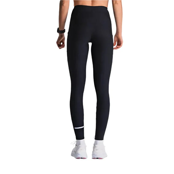 En person iført Fusion X-Long Training Tight, Dame, SuperBlack-leggings, en sort fitness-tracker og hvide sportssko står med ansigtet vendt mod kameraet på en hvid baggrund.
