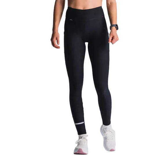 En person er iført Fusion Hot Long Tights, Dame, Black med en lille refleksstribe på venstre ben, parret med hvide løbesko og et fitnessur, og står på en almindelig lys baggrund.