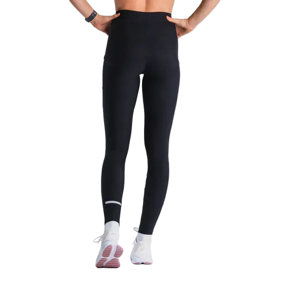 En person står baglæns iført Fusion Hot Long Tights, Dame, sorte og hvide sportssko med pink såler samt et armbåndsur. Baggrunden er ensfarvet og lys.