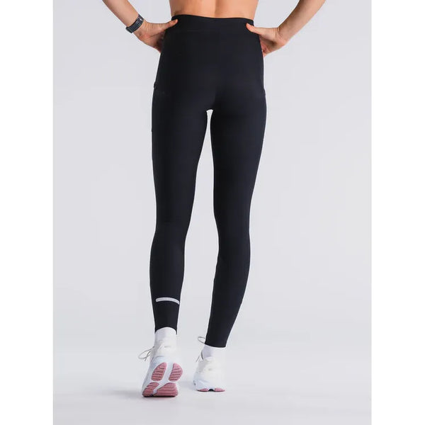 Modellen ses bagfra iført Fusion Hot X-Long Tights, Dame, Black med reflekterende ankelstribe og hvide sportssko på en almindelig hvid baggrund.