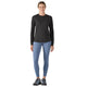En kvinde står med front mod en hvid baggrund iført en Patagonia L/S Cap Cool Merino Blend Graphic Shirt i sort, lyseblå leggings og sorte sportssko.