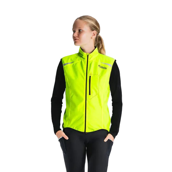 En person står let vendt og er iført Fusion S1 Run Vest til kvinder i gul over en sort langærmet skjorte og bukser på en almindelig lysegrå baggrund.