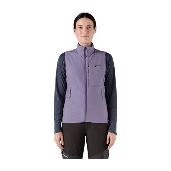 En person står med ansigtet fremad i en Patagonia W's Nano-Air Light Vest til kvinder i Concrete Purple, over en langærmet mørk skjorte og sorte bukser, klar til bjergtræning mod en almindelig hvid baggrund.
