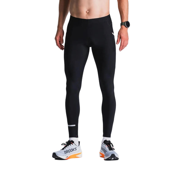 En person står i bar overkrop mod en hvid baggrund iført Fusion X-Long Tights Unisex i SuperBlack; ansigtet er ikke synligt. Vedkommende bærer også et sort armbåndsur og hvide Brooks-løbesko.