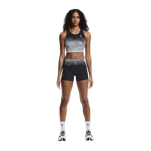 En person står med ansigtet fremad og er iført On Zero Short Tights, Dame, Black/White med en sportsbh med gradient, hvide ankelsokker og hvide løbesko på en almindelig hvid baggrund.