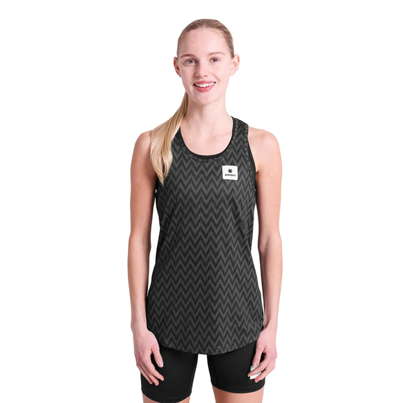 En person med langt blondt hår bundet tilbage smiler fremad, iført Saysky Zig Zag Combat Singlet, Dame, Black Zigzag, med sorte shorts på en almindelig hvid baggrund.