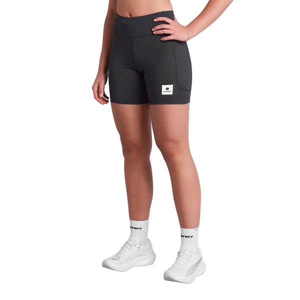 Iført Saysky Zig Zag Combat+ Short Tights 7" i Black Zigzag, hvide FLEXY-sokker og hvide sneakers ses en person fra taljen og ned med den ene hånd på hoften og den anden afslappet.